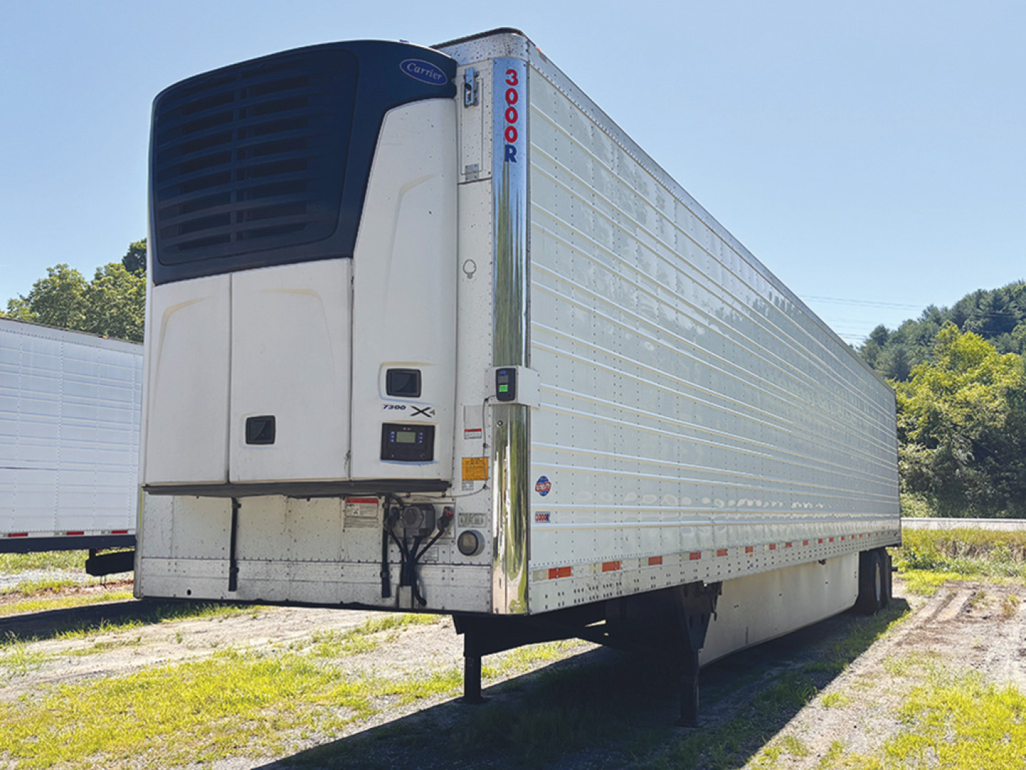 Utility reefer trailer with Thermo King unit at the front showing a vertical 1000R id on the nose; side walls are ribbed aluminum; rear doors visible; trailer parked on a gravel lot.