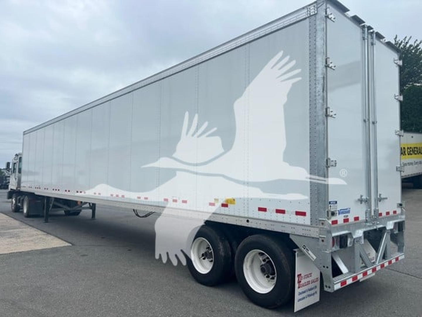 Trailer side view showing large white bird graphic on silver Vanguard VXP plate trailer with dual rear tires and back doors.