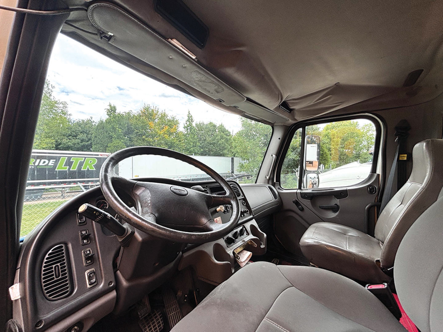 Cab interior of a Freightliner M2 106 with steering wheel, dashboard, and seats visible.