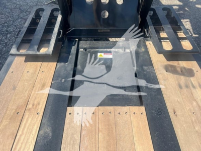 Lowboy trailer deck view with forklift attachment and wooden deck planks, black frame rails, and fork pockets.