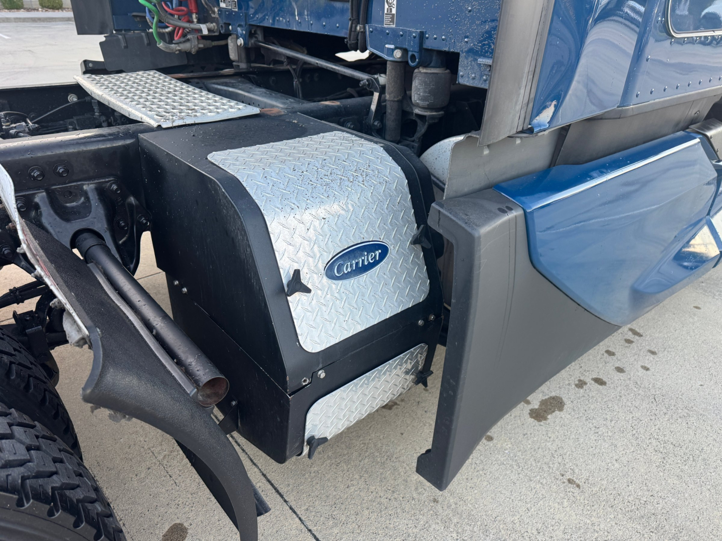 Kenworth T680 engine bay area showing Carrier auxiliary component with diamond plate cover and blue body panel.