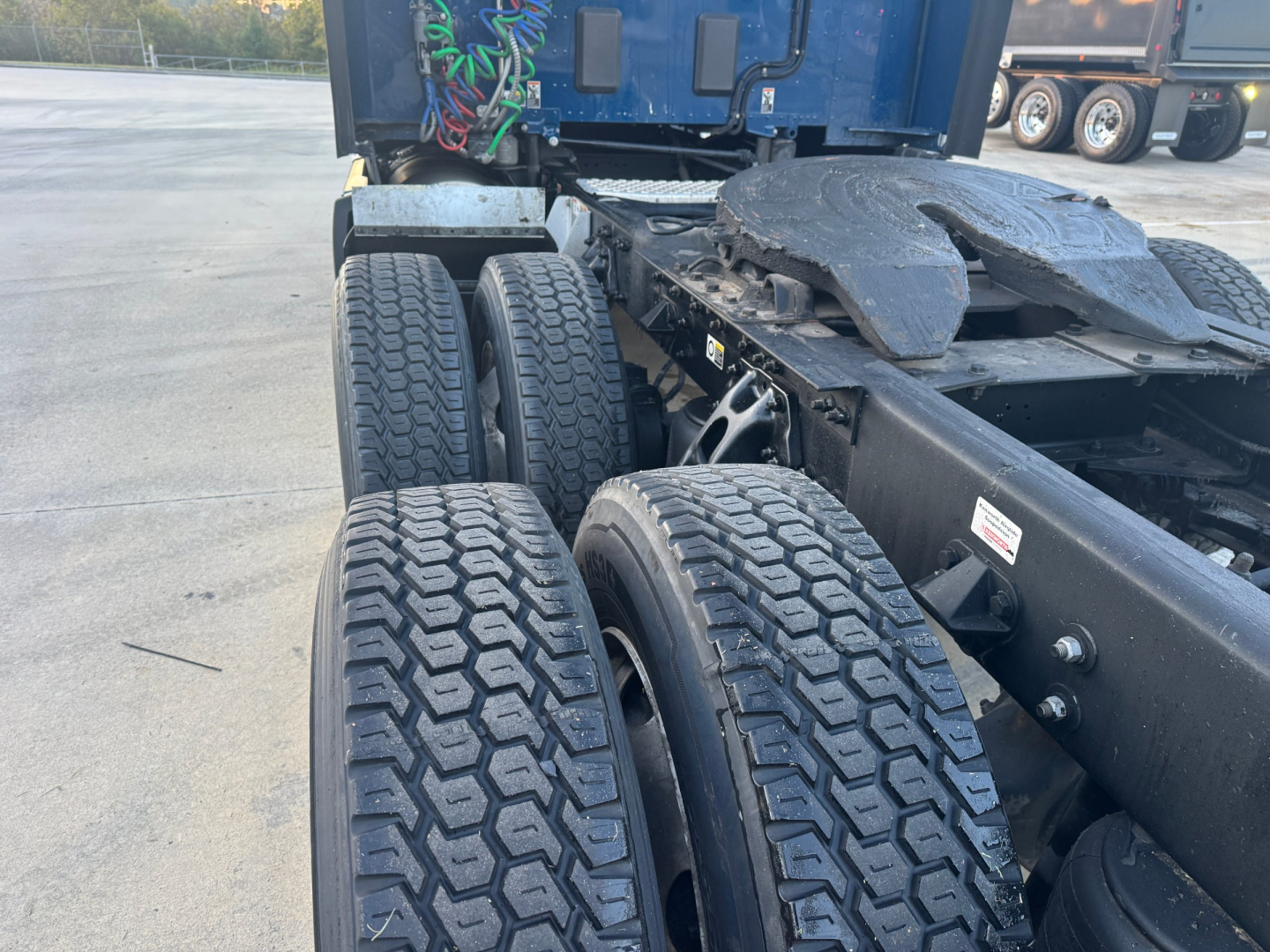 Kenworth T680 drivetrain area showing dual rear axles with large tread tires and frame rails, cab interior wiring visible in background.