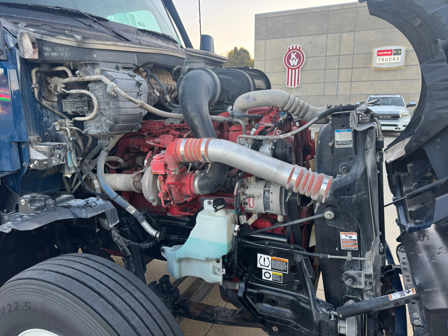 Kenworth T680 engine bay showing red engine block, hoses, coolant reservoir, and various labeled components.