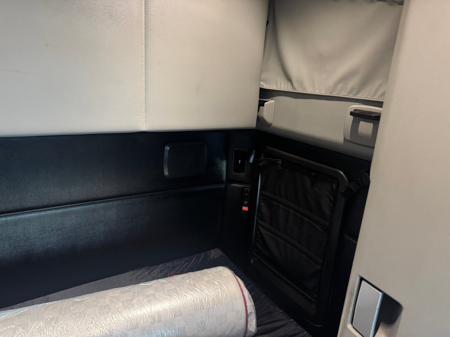 Cab interior of a 2024 Kenworth T680 sleeper-tractor showing padded wall, storage net, and window shade.
