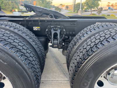 Kenworth T680 chassis view showing dual rear axles and fifth-wheel mounting area with various labels. Visible text includes warning label on left side and structural components.