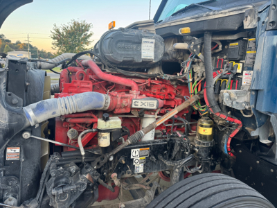 Kenworth T680 engine bay showing X15 engine with red components, hoses, and exposed wiring in the cab-forward area.