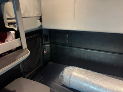 Kenworth T680 interior cargo area showing sleeper cab side panel and folded mattress/foam roll in plastic.