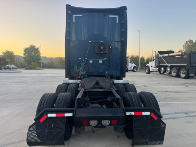 Kenworth truck chassis rear view showing fifth wheel, dual rear axles, mud flaps, and taillights. Visible components include bumper with reflectors and license plate area.