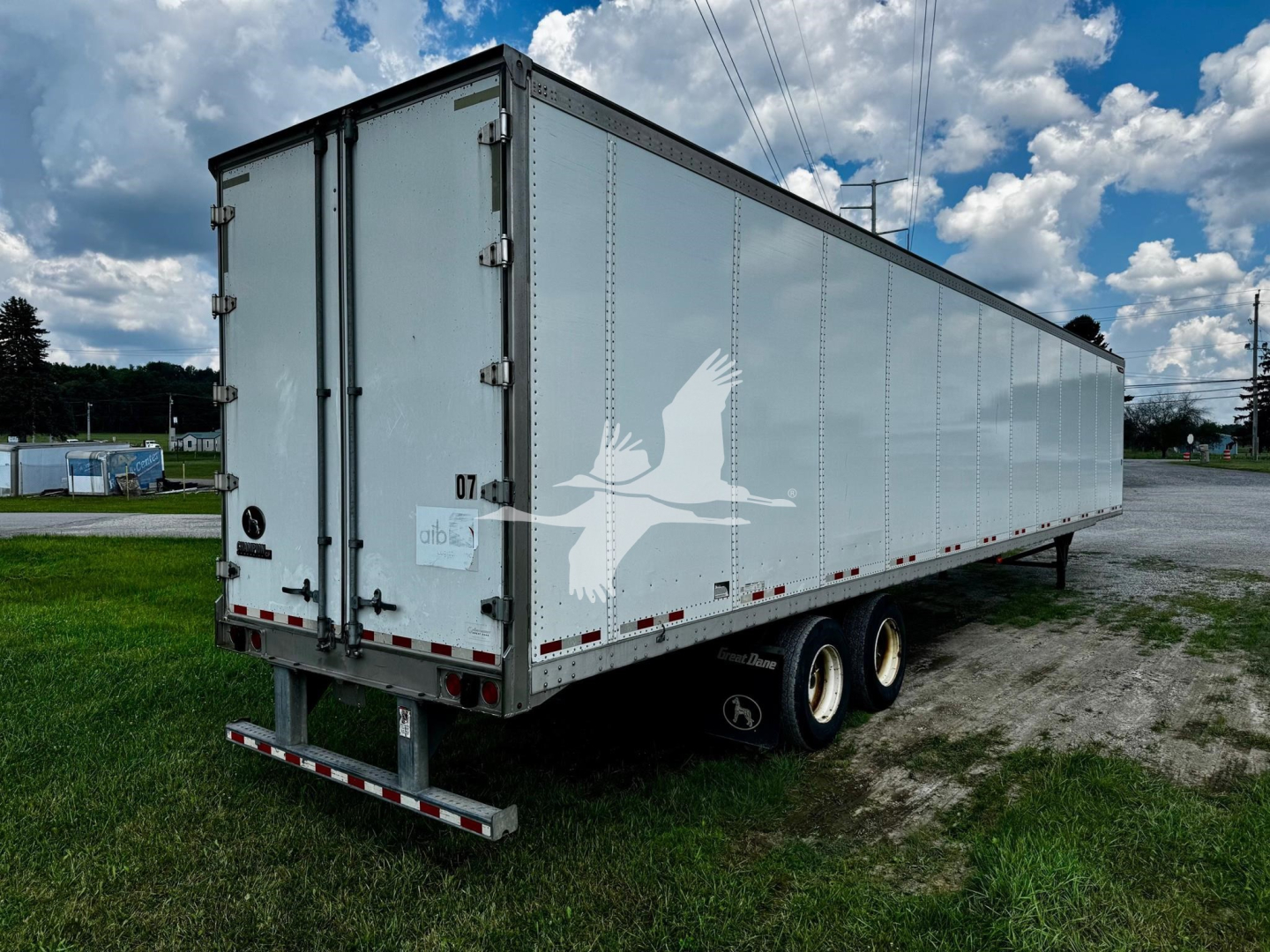 Great Dane plate trailer with tandem axle showing side and rear doors; white exterior with a large bird graphic on the side; taillights and safety reflectors along lower edge; rear doors closed.