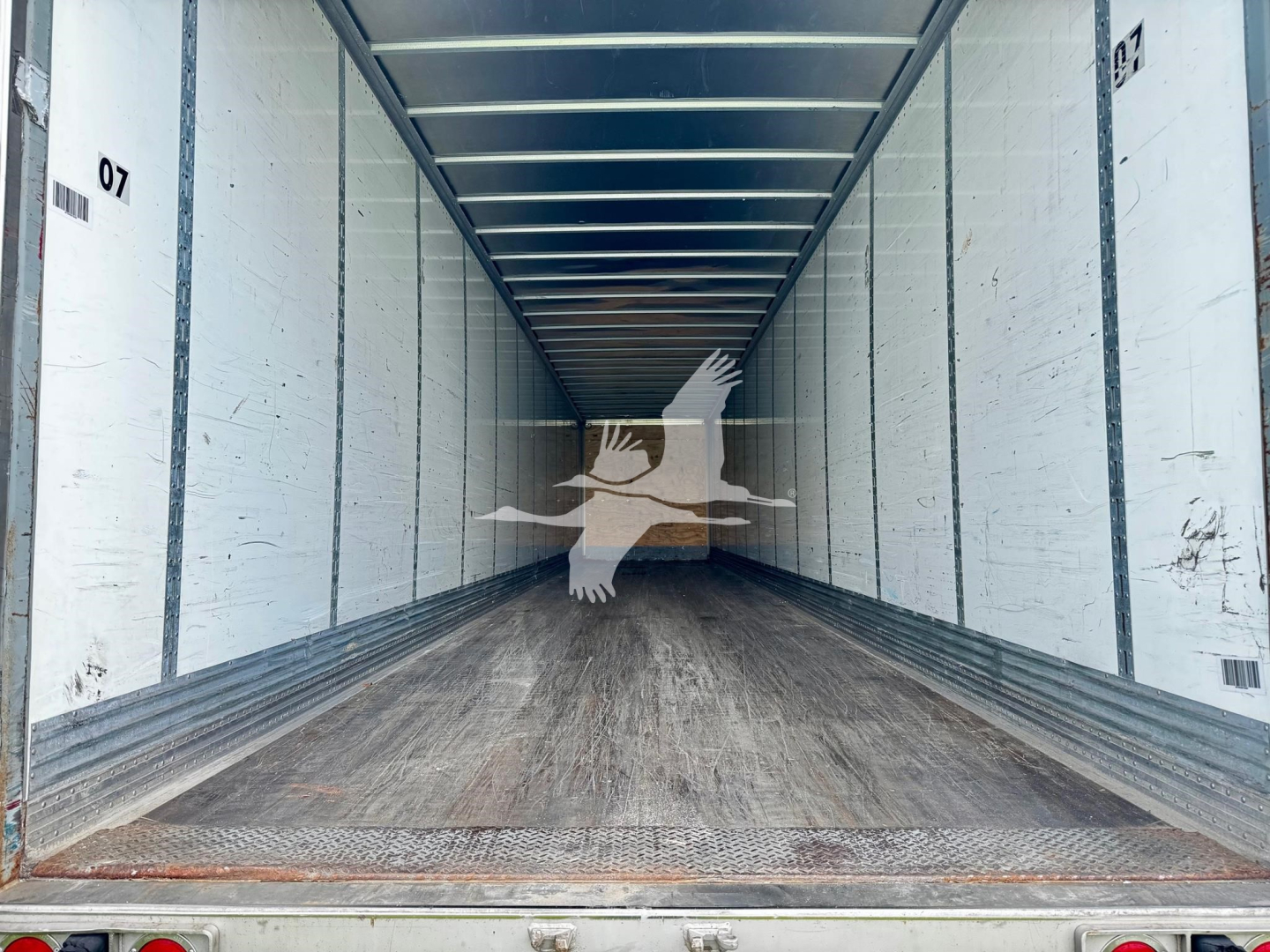 Great Dane plate van trailer interior showing empty cargo bay with wooden floor and white side walls, overhead ceiling beams.