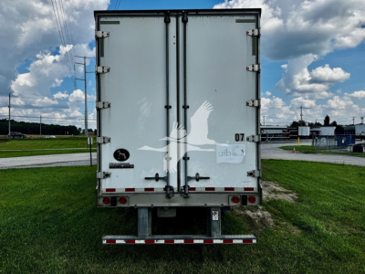 Rear view of a white Great Dane plate trailer with double doors, taillights, and bumper; VIN tag and stock number area not visible.