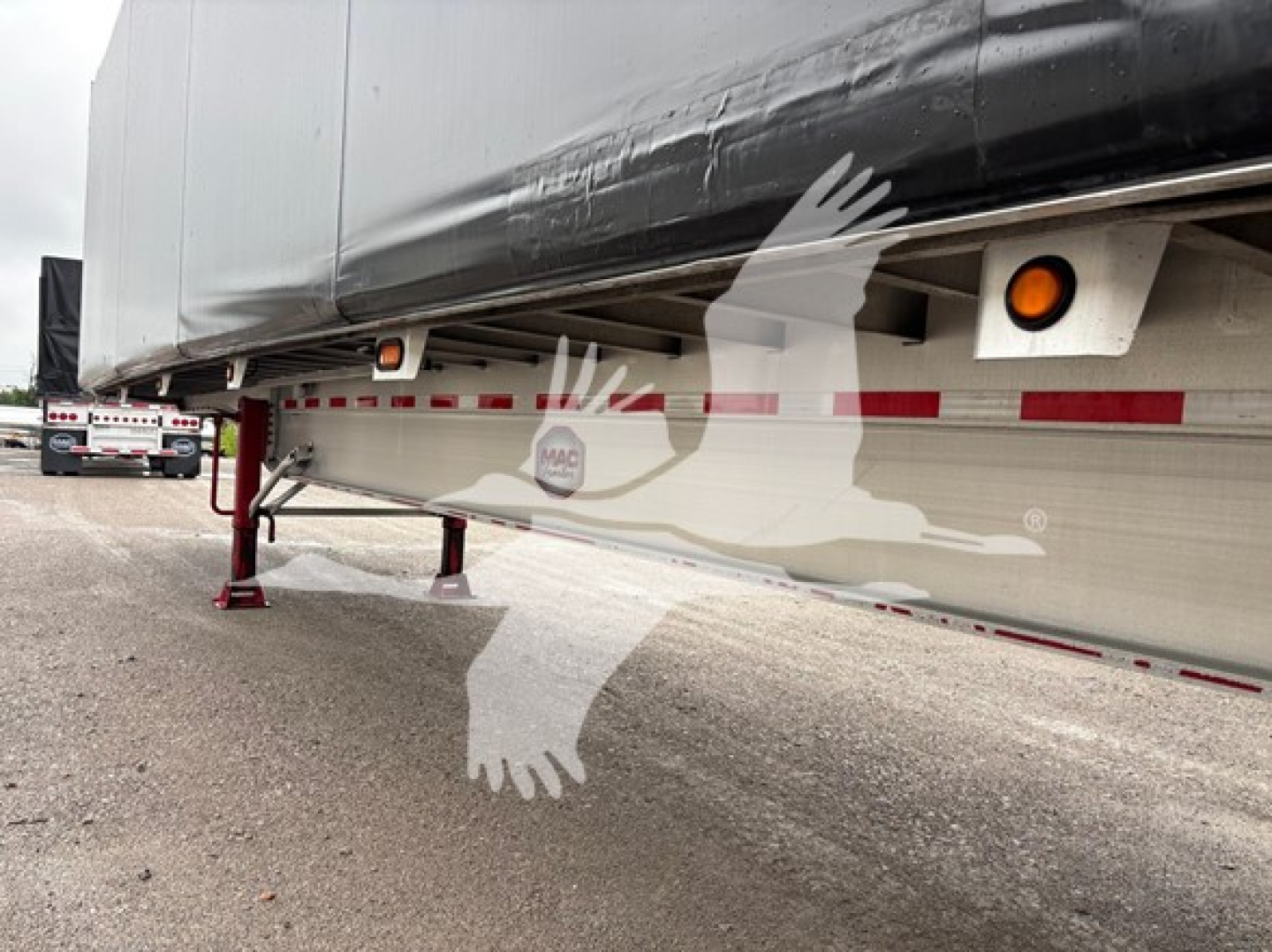 Trailer undercarriage showing side rail with reflectors and landing gear, MAC trailer logo visible on side, low angle view of curtainside trailer.