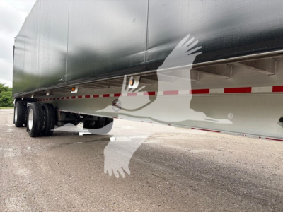 Trailer undercarriage side view showing axles and tires, with reflection and a white stylized bird watermark overlapped on the lower body.