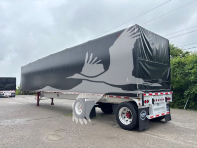 Curtainside trailer in profile showing a large black tarp with a white bird graphic and rear lights.