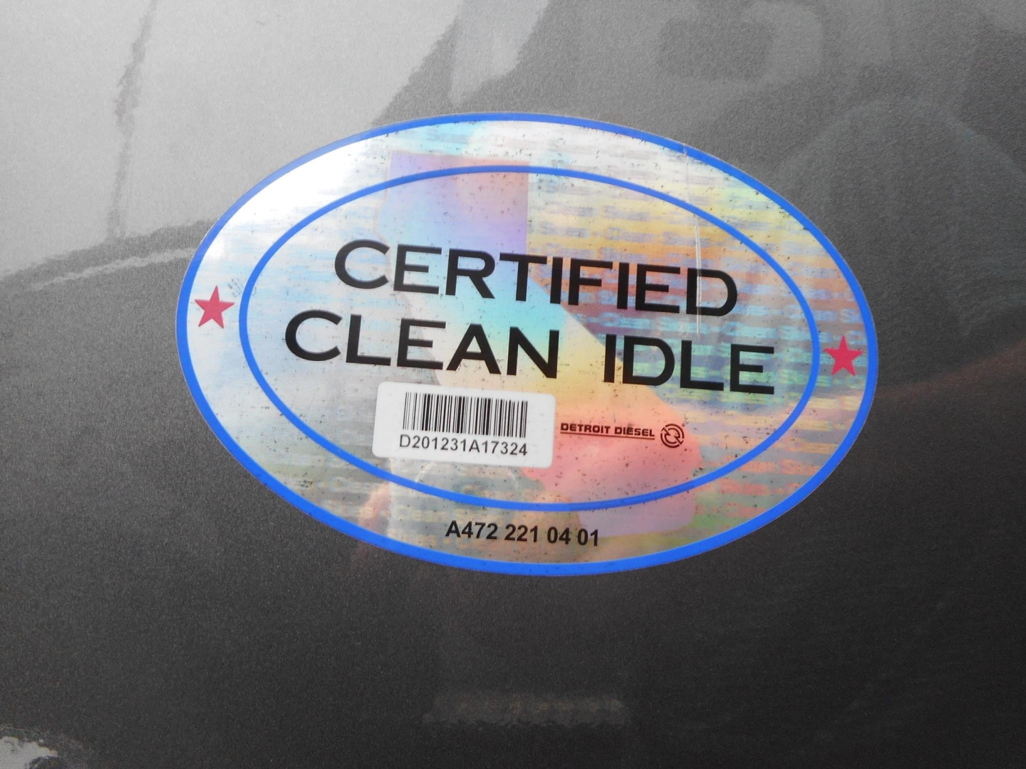 Fleet sticker on dark truck surface reading CERTIFIED CLEAN IDLE with holographic design and barcode sticker beneath.