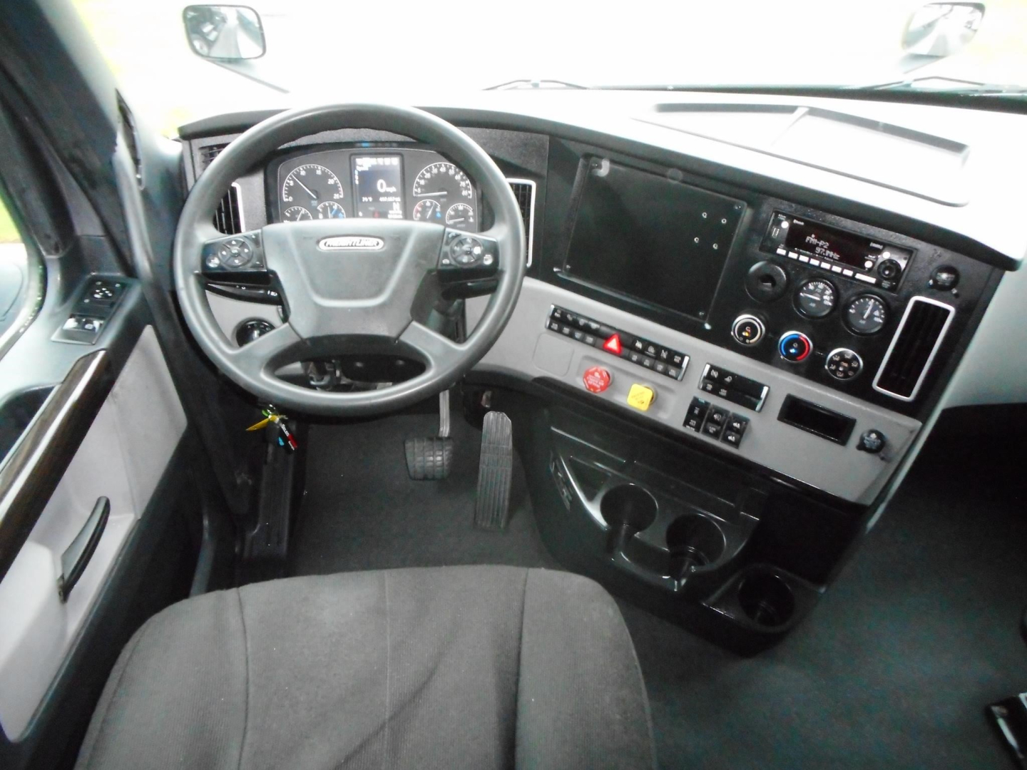 Cab interior of a Freightliner Cascadia 126 with steering wheel, dashboard, and center console showing gauges, touchscreen, and controls.