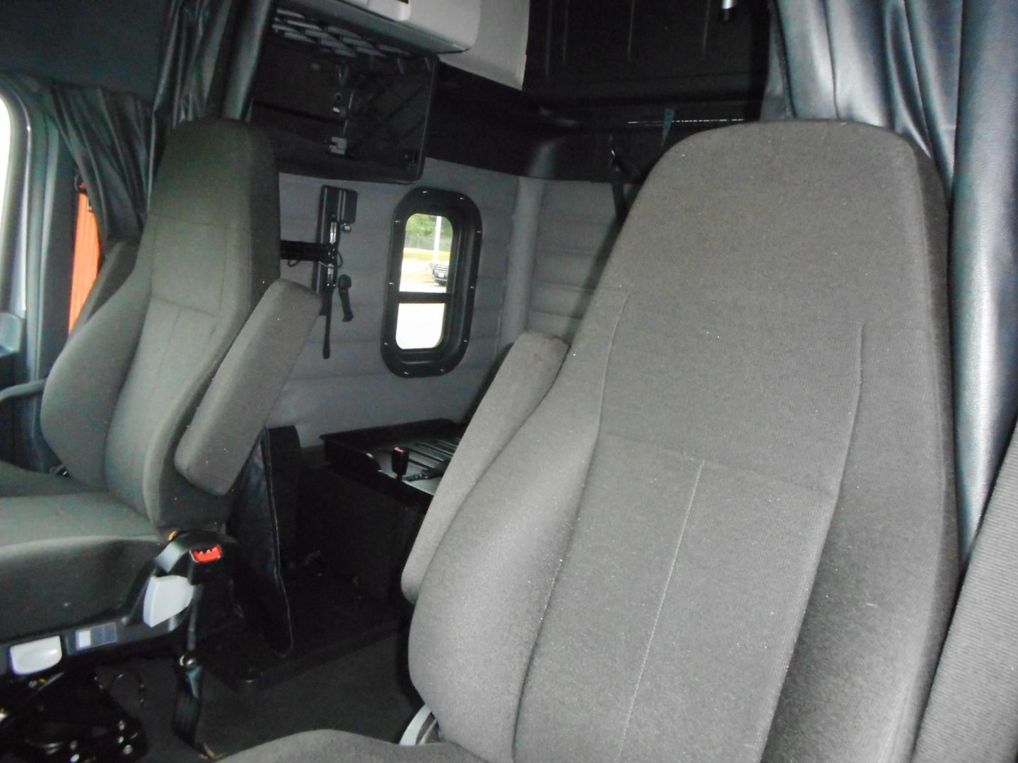 Interior cab seating area of a Freightliner Cascadia 126 truck showing front and side seats with storage compartments and window.