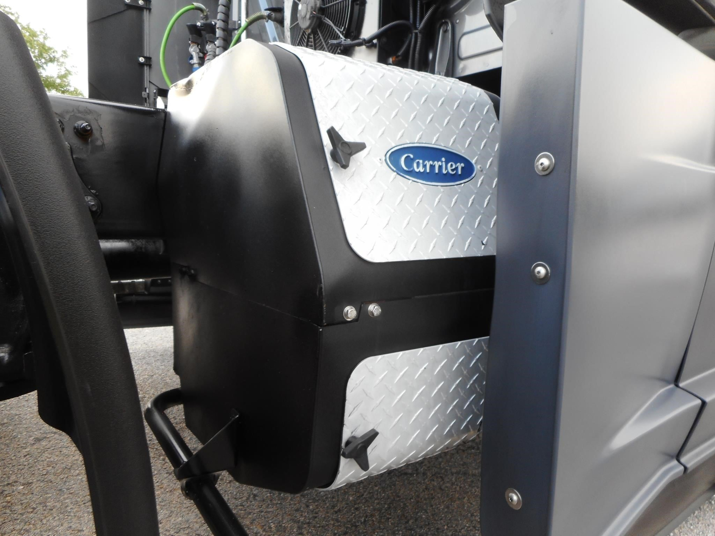 Carrier logo on the side of a pickup-style silver diamond-plate fuel tank mounted on a Freightliner Cascadia 126 truck engine area.