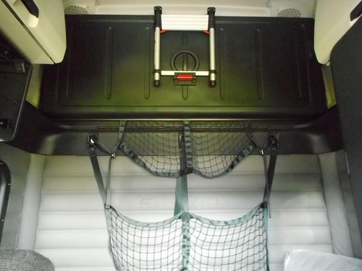 Cargo area of a Freightliner Cascadia 126 interior showing overhead storage hatch and netted cargo organizer.