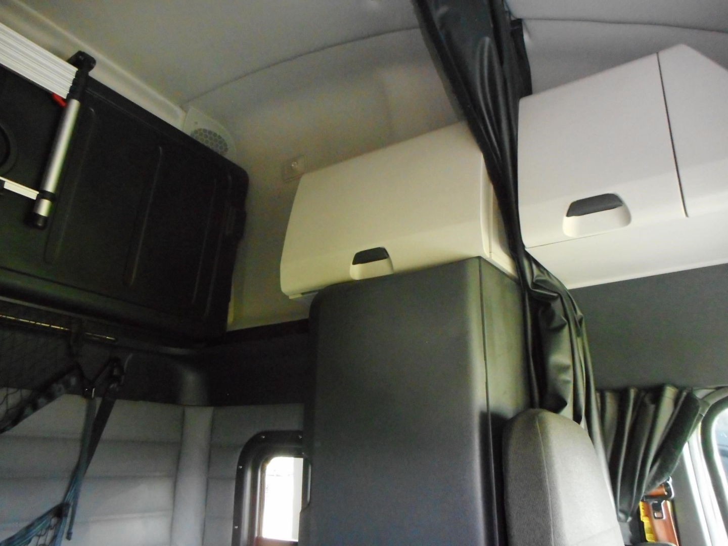 Cab interior overhead storage compartments and cables in a Freightliner Cascadia sleeper cab, with black toolbox and white cabinets near the ceiling.