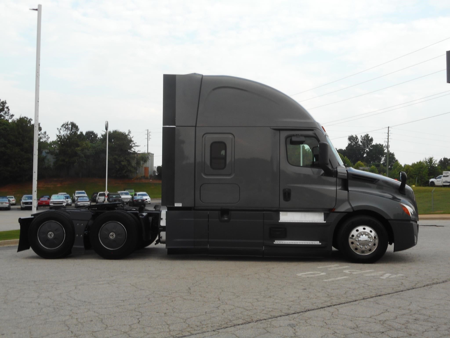 Truck side view of a 2022 Freightliner Cascadia 126 sleeper cab tractor in grey, with dual rear axles and chrome wheels.