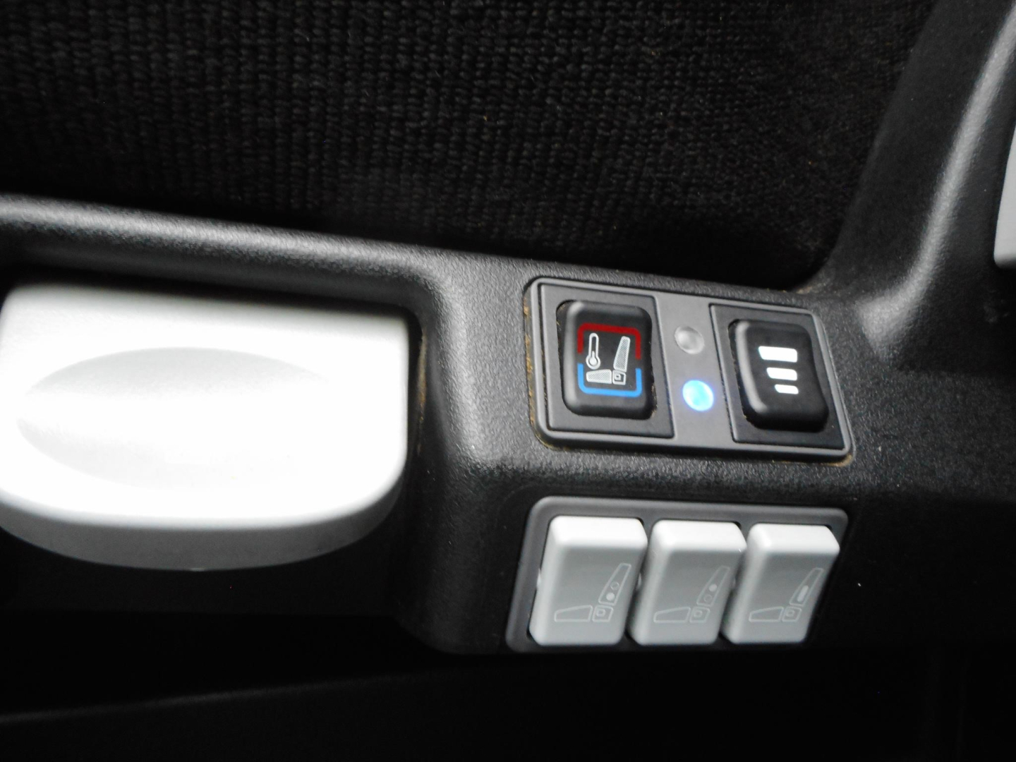 Seat heater switch and three memory/seat controls in Freightliner Cascadia cabin area with light blue indicator and white icons.