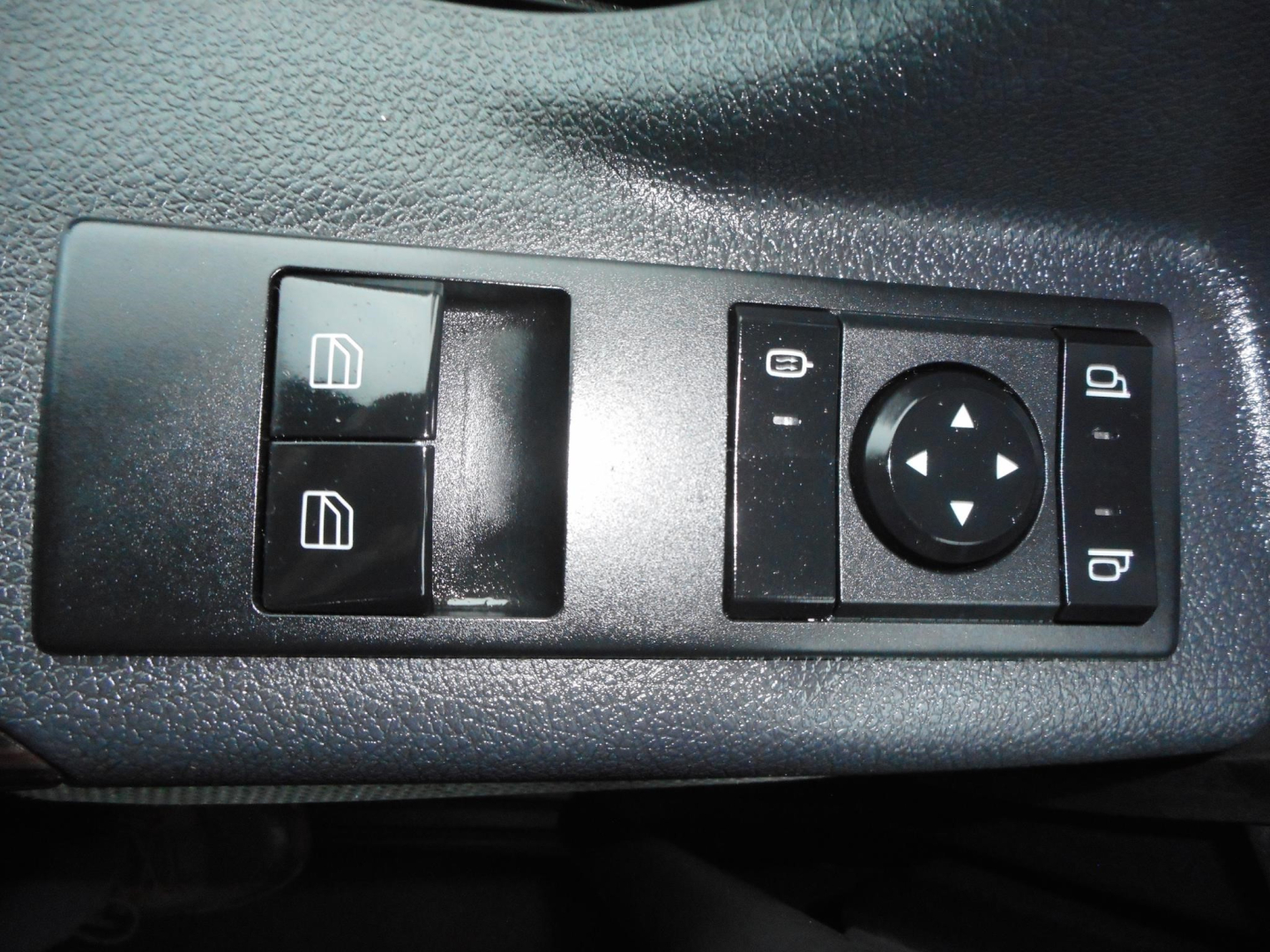 Truck interior control panel with window switches and mirror control dial. Shows two window switches on left and a round joystick-like control with directional arrows on right, plus vertical buttons.
