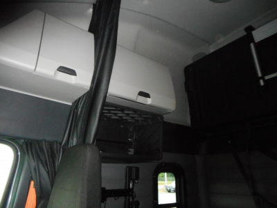 Cab interior of a Freightliner Cascadia sleeper showing overhead storage compartments and passenger area. 