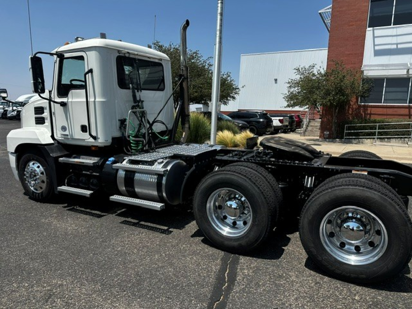 Truck cab and dual rear axles of a Mack ANTHEM tractor in a dealership lot, side view showing chrome fuel tanks and steps.