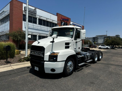 White 2020 Mack Anthem Conventional Daycab tractor in front of dealership showing Mack grille and fuel tanks.