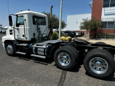 Truck cab and dual rear axles of a Mack ANTHEM tractor in a dealership lot, side view showing chrome fuel tanks and steps.