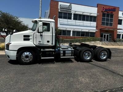 Truck chassis of a white 2020 Mack Anthem daycab visible from side, with dealership building in background.