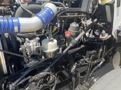 Kenworth T800 engine bay showing blue silicone intake hose, multiple hydraulic lines, battery, and various reservoirs and components.