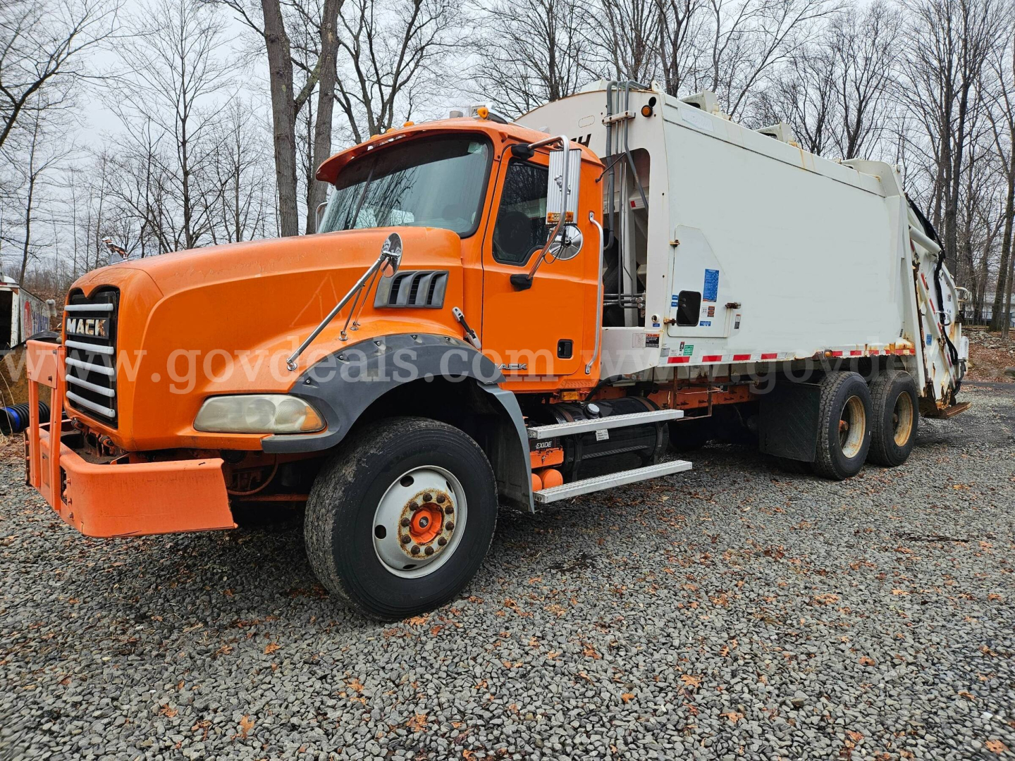 Mack GU813 garbage truck showing bright orange cab and white rear body with side mirrors and large front bumper.