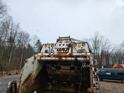 Mack GU813 garbage truck rear showing rusted body, hydraulic components, and rear hopper with Leach branding visible.