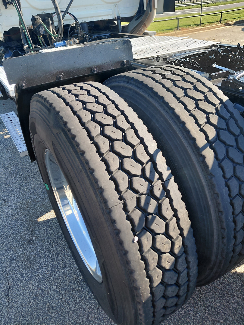 Truck rear dual tires and chassis with fuel lines and components visible in the engine bay area.