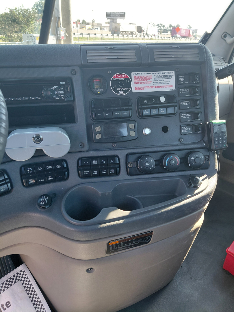Dashboard controls and instrument panel of a Freightliner truck cab showing multiple gauges, switches, and vents.