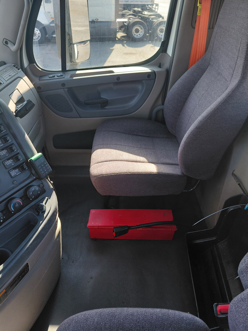 Cab interior of Freightliner PT126064S showing driver seat, dashboard, and a red toolbox on the floor.