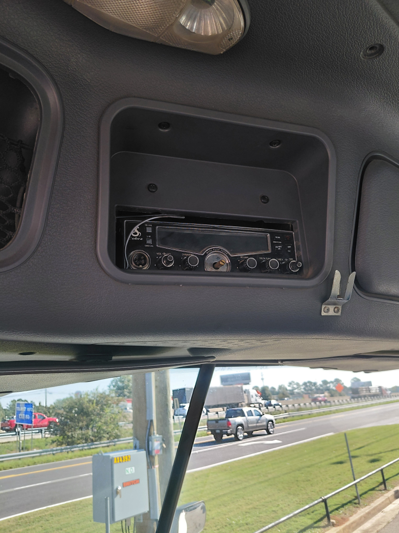 Dashboard area showing a radio head unit installed in a recessed panel under overhead storage of a Freightliner truck cab.