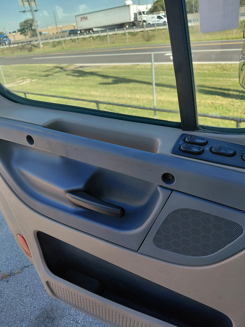 Truck interior door panel and window frame of a Freightliner PT126064S T cab showing interior door handle, window switch area, and speaker/grille.