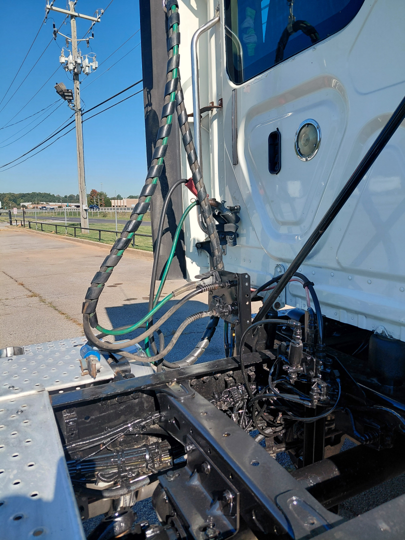 Truck cab area showing exposed wiring harnesses and connection points behind the sleeper, with metal steps and hitch area visible.