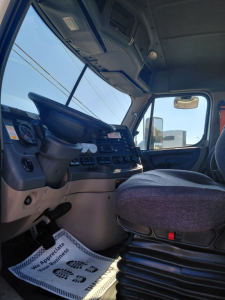 Truck cab interior with steering wheel and seat, dashboard controls visible.