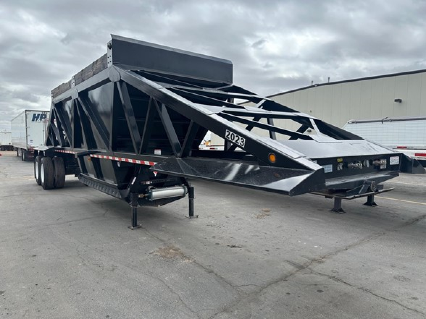 Bottom dump trailer by Brazos with air ride suspension, black steel truss frame, front hopper, dual axles, ramp bed, and identification label 2023 on frame.