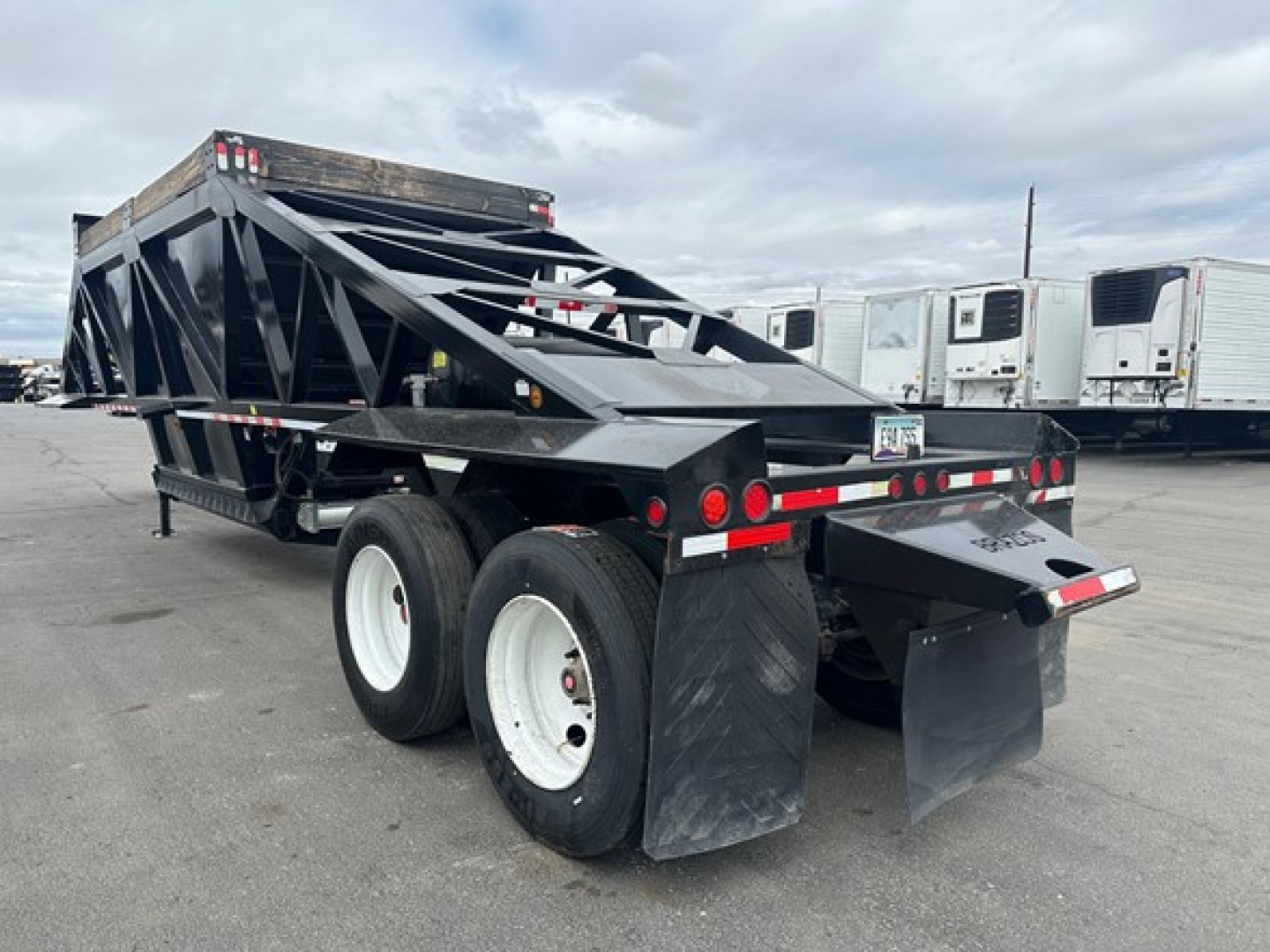 Bottom dump trailer showing dual rear axles with mud flaps and black steel framing, rear ramp/door and reflective tape along sides.