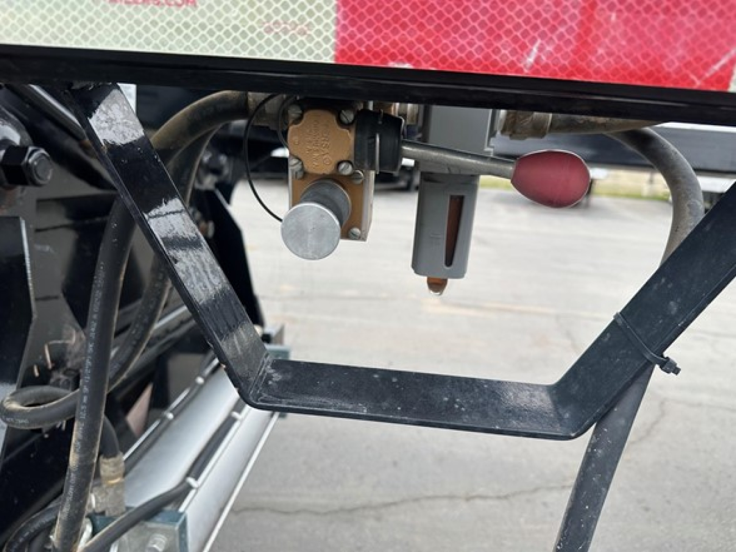 Bottom dump trailer detail showing hydraulic valve and latch components under a Brazos air ride bottom dump. Visible F-Hose fittings, metal frame, and hydraulic actuator mount.