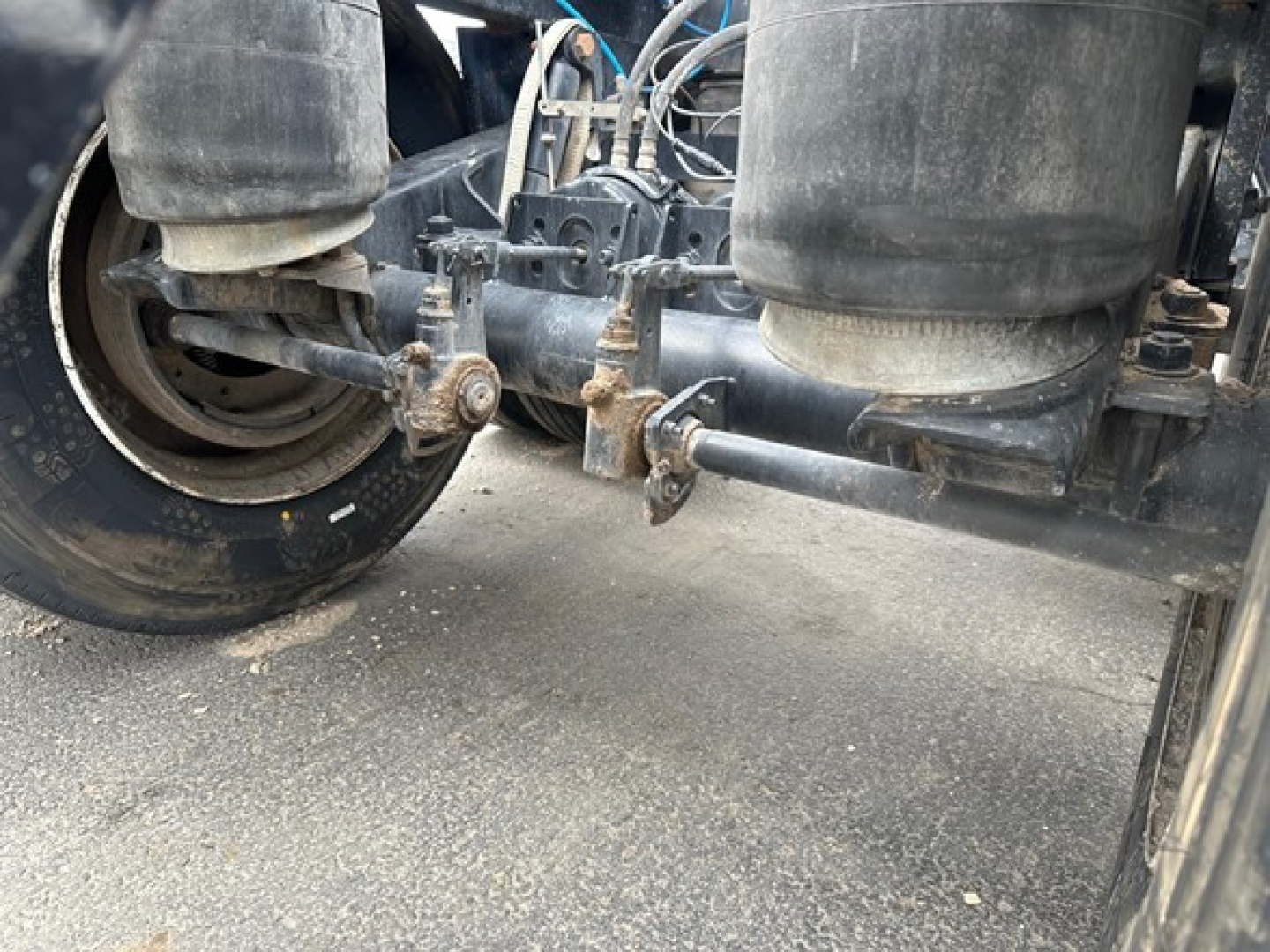 Bottom dump trailer undercarriage showing suspension air bags, axle, and linkage with visible bolts and frame.