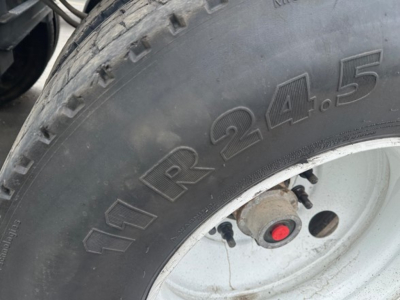 Tire close-up showing tread and embossed marking 11R24.5 on sidewall of Brazos trailer wheel, with rim and brake drum visible.