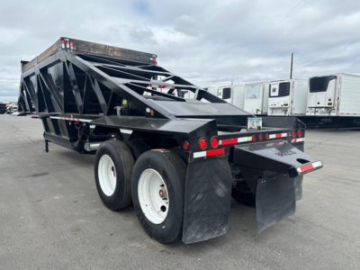 Bottom dump trailer showing dual rear axles with mud flaps and black steel framing, rear ramp/door and reflective tape along sides.