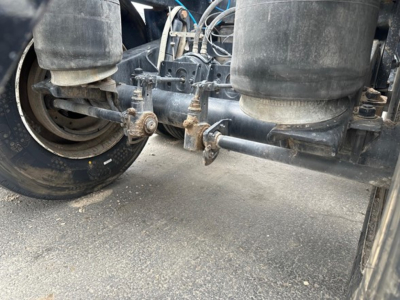 Bottom dump trailer undercarriage showing suspension air bags, axle, and linkage with visible bolts and frame.
