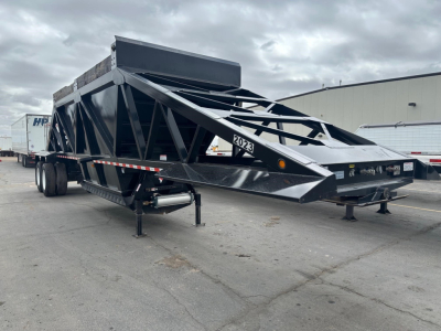 Brazos bottom dump trailer in view showing structural lattice frame, dual axle, and front hopper. Visible text includes '2023' on the side panel and a sticker with the number.